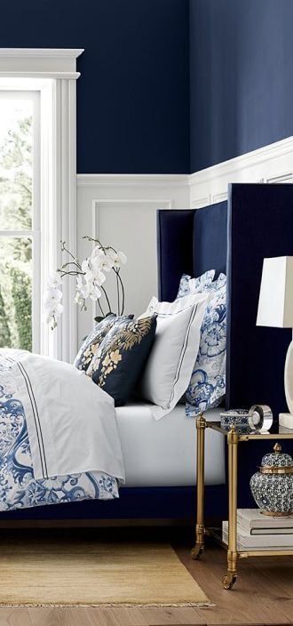 blue and white bedroom set up in a classic design scheme with orchids next to the window and a brass bed side table 