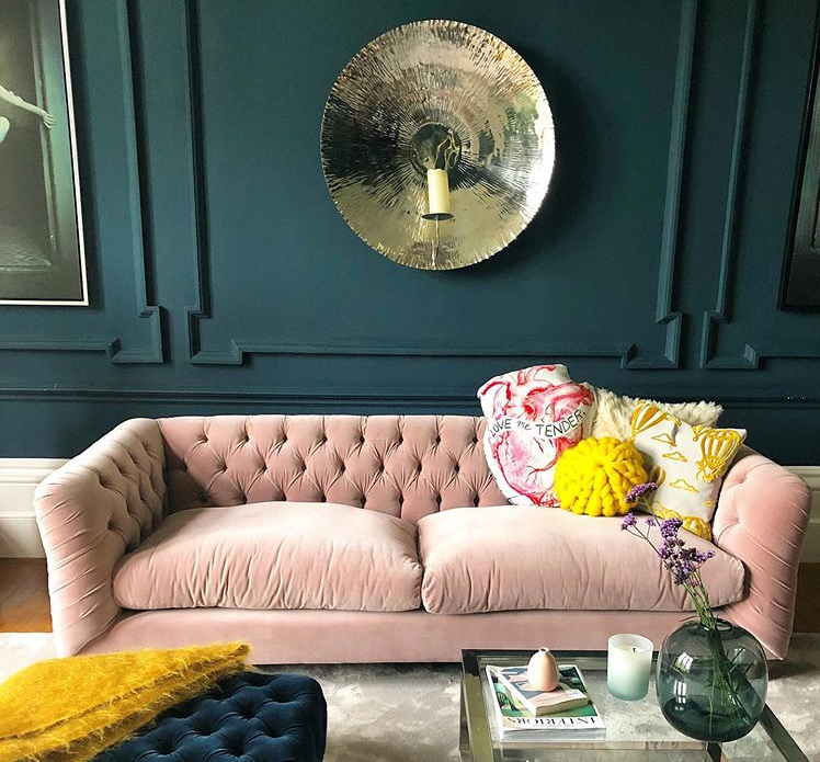 Dark living room with soft pink sofa with yellow accessories and a large metallic wall hanging