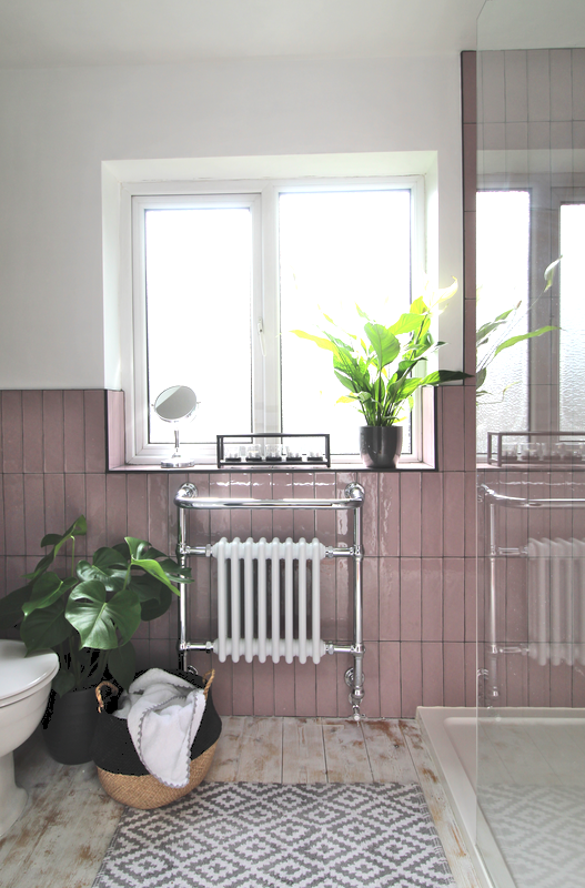 traditional towel radiator within the bathroom keeps the space warm and a practical place to hang towels. pink tiles, grey grout and weather boarded floors