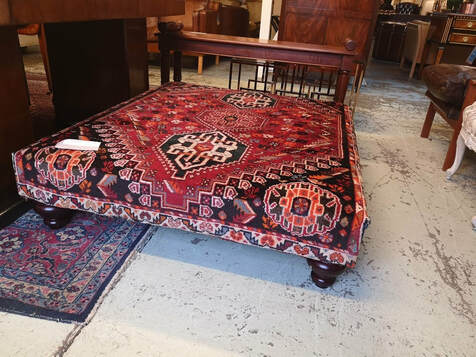 an uphlstered foot stool in a carpeting type fabric with the pattern of a persian carpet