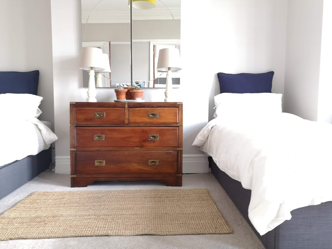 a twin bedroom with blue and grey scheme and antique campaign style chest of drawers