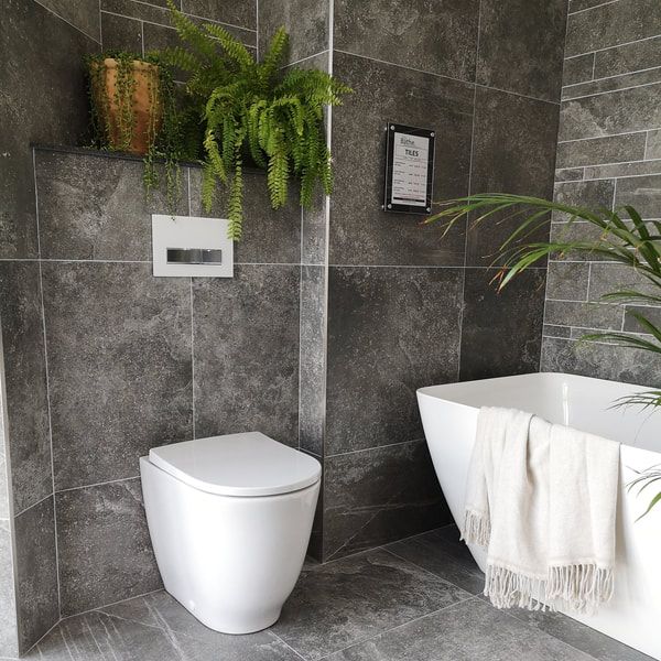styled bathroom with a towel over the bath, and lovely green palm and plants in the room. Geberit dual flush plate show how versatile it can be
