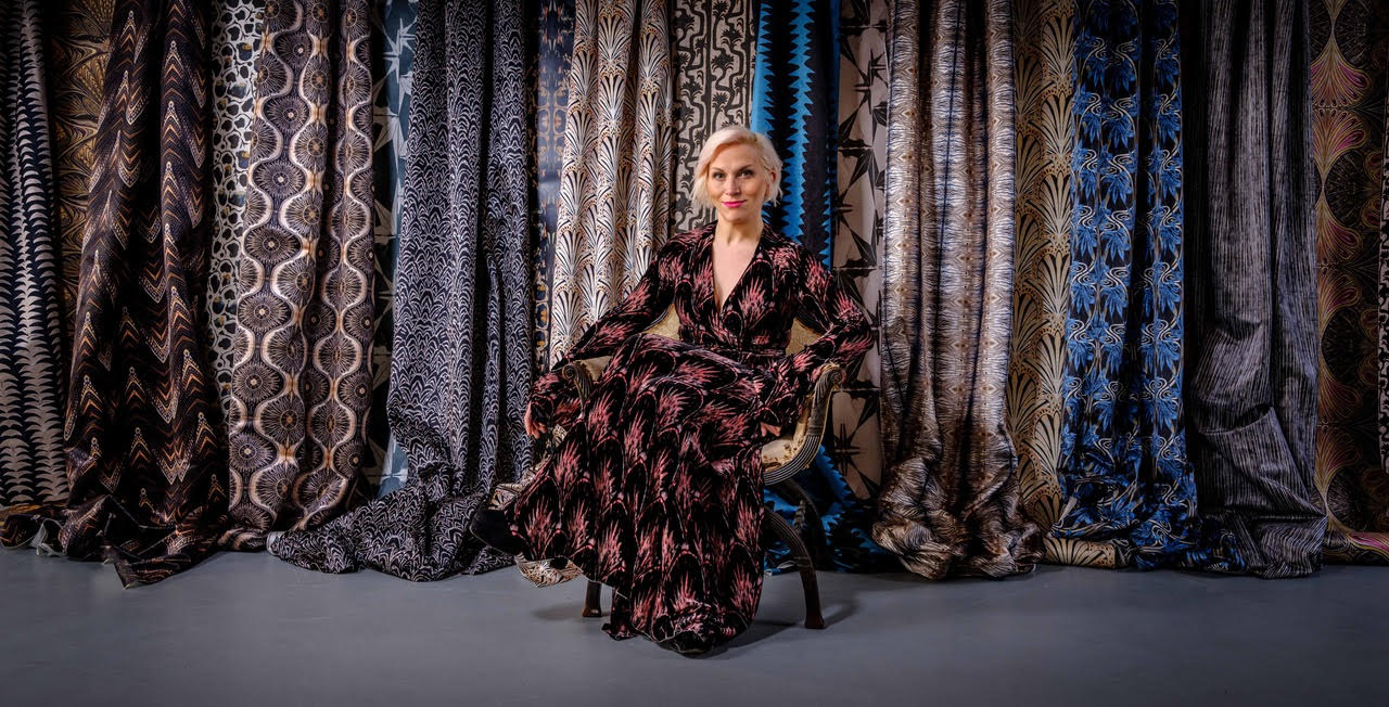 Anna Hayman sat in front of a wall full of her patterned fabrics wearing one of her own designs