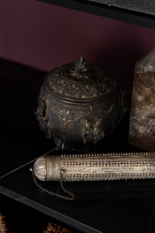 vigniette of decorative accesories, a tibetian prayer pot, a yemeni silver scroll holder and a crystal obelisk.