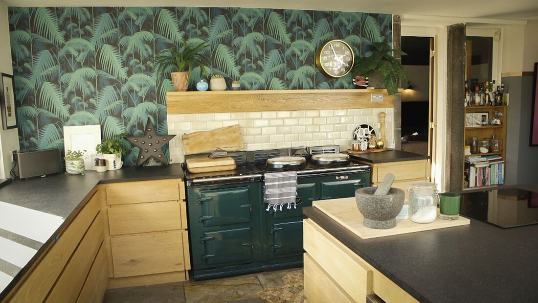 oak kitchen with a dark slate countertop with a green palm wallpaper