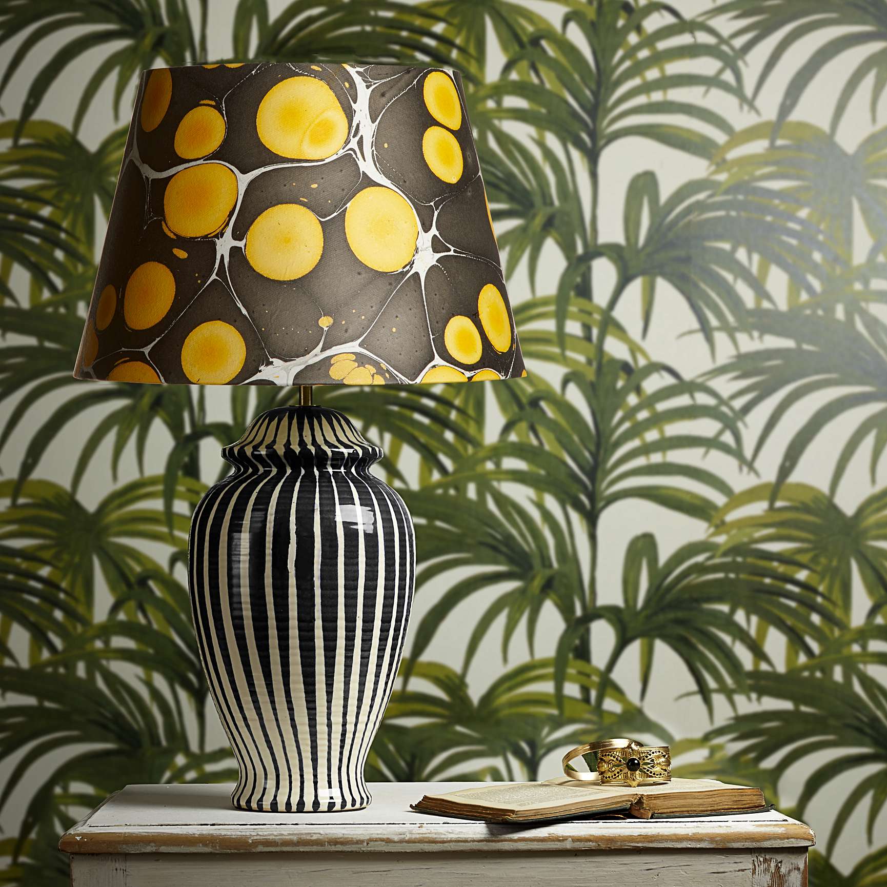 black and white stripy lamp base with a black and gold marbleized paper shade against a palm print backdrop