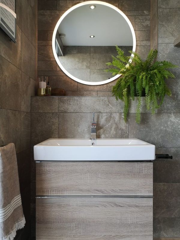 styled photo of a backlit mirror in a bathroom showing the acanto range and greenery and candles in a bathroom all creating a sensory space
