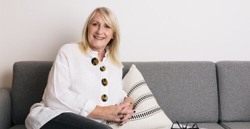 Helen Orrock in a white linen top on her sleek modern sofa