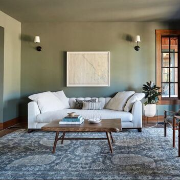 Living room painted green with a white vintage sofa and an off centre painting with a vintage rug.