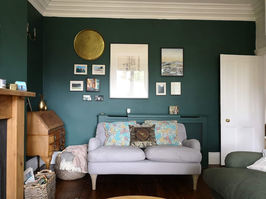 gallery wall of mixed art pieces including sculpture, prints and paintings set against a dark green wall above a pale grey sofa.