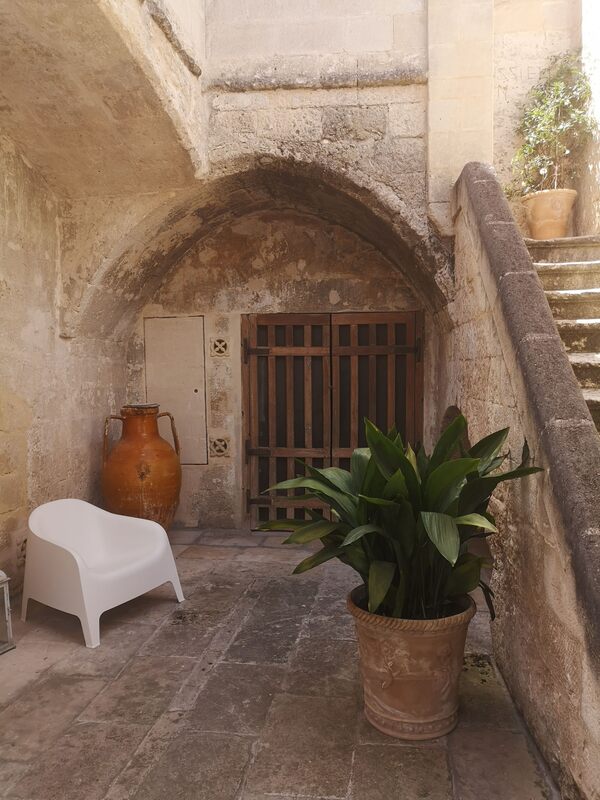 Italian courtyard with large urns and plants with a white chair in the corner and an open staircase with a pointed gothic arch
