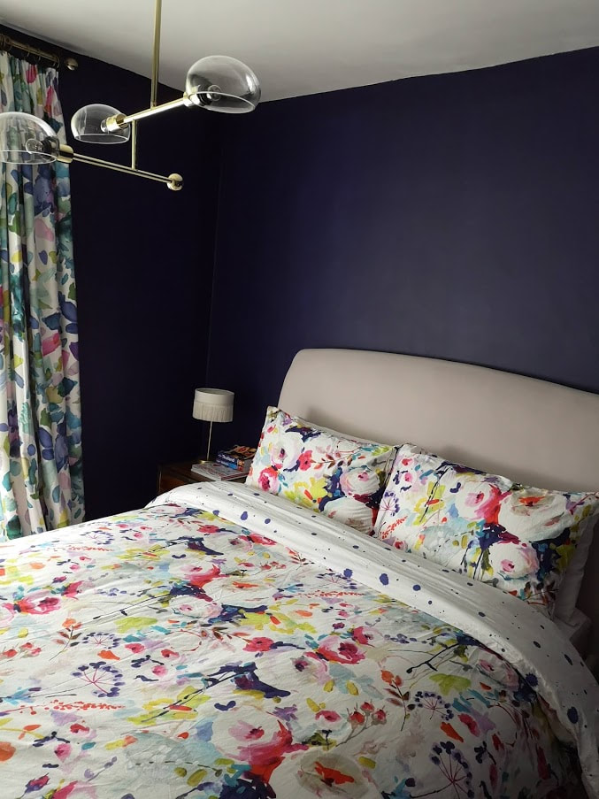 Dark blue bedroom with floral bed sheets and gold accessories and details 