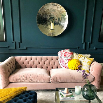 Dark blue living room with a large metal wall hanging and a pink velvet sofa